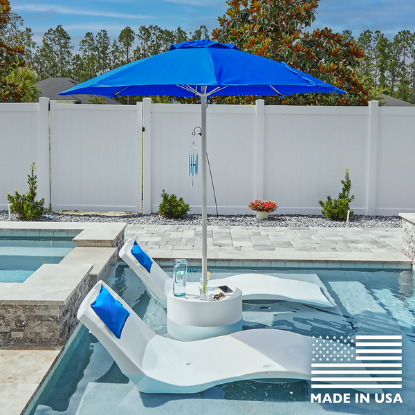 White lounge chairs with blue cushions under a blue umbrella by a pool, with 'Made in USA' label.